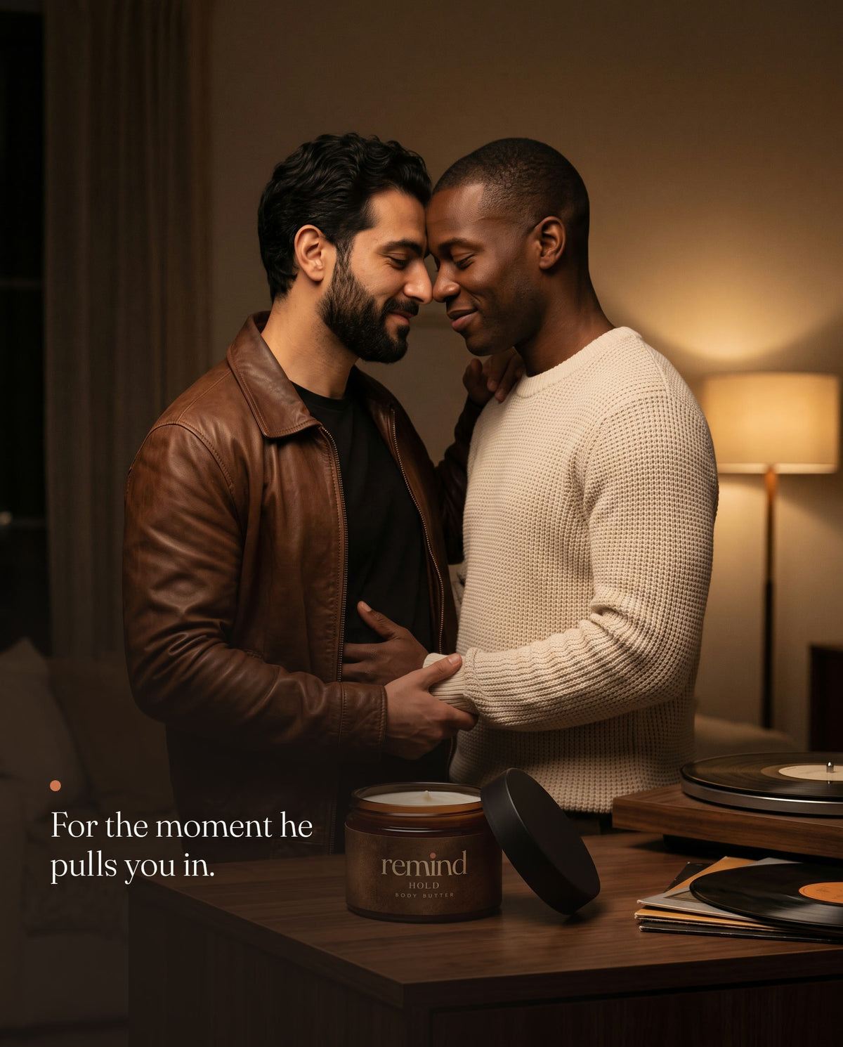 Two men slow-dancing in a lamplit living room, foreheads together; an open jar of REMIND HOLD body butter on the sideboard. Caption: For the moment he pulls you in.
